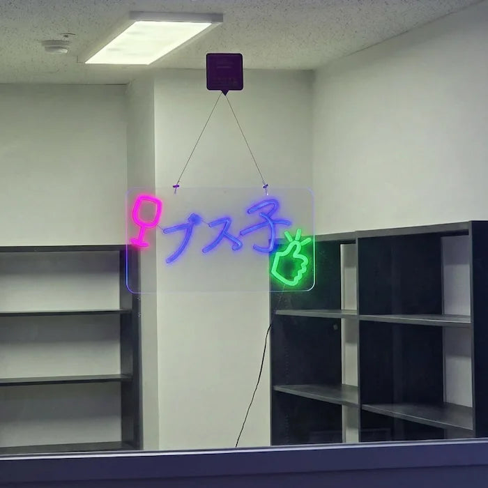 ブス子ロゴのLEDネオンサイン看板。窓ガラスタイプをガラスに設置した状態で点灯し、正面から撮影した全体写真。