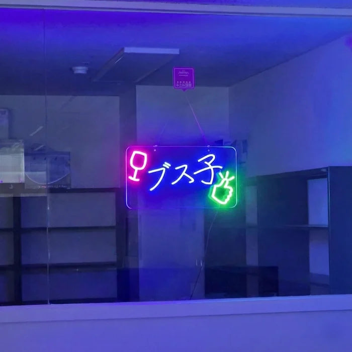 ブス子ロゴのLEDネオンサイン看板。窓ガラスタイプを薄暗い背景をバックに点灯し、正面からクローズアップして撮影した全体写真。