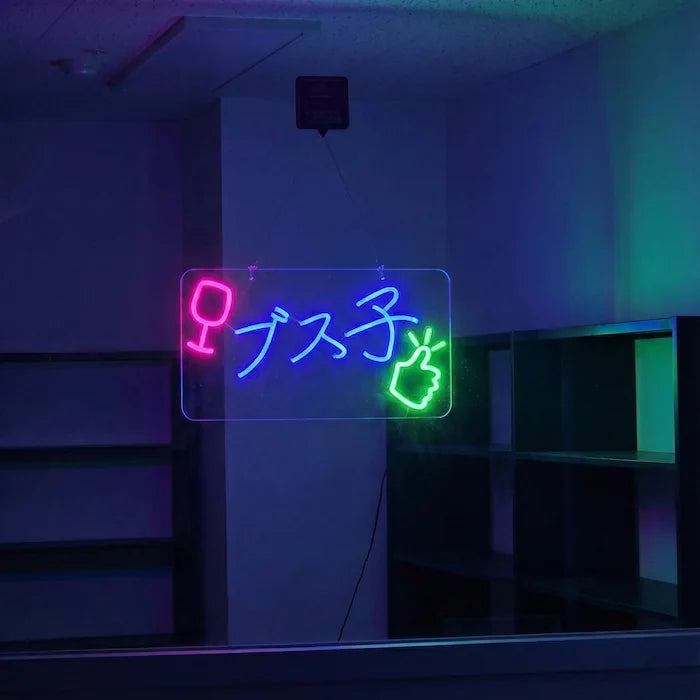 ブス子ロゴのLEDネオンサイン看板。窓ガラスタイプを薄暗い背景をバックに点灯し、正面から撮影した全体写真。
