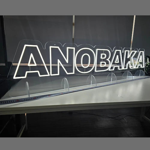 ANOBAKAロゴのLEDネオンサイン看板。アクリル立て台で立つスタンドタイプを点灯して左斜めから撮影したアングル。