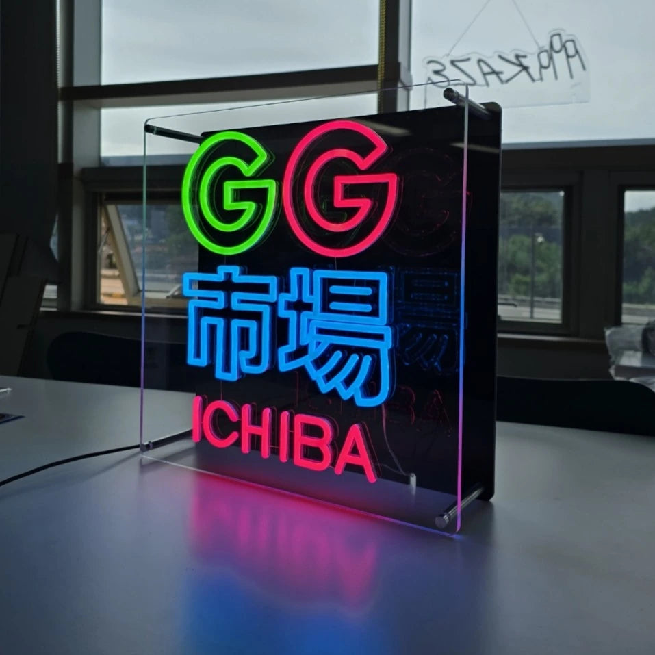 GG市場ロゴのLEDネオンサイン看板。金属スペーサーと２枚のアクリル板で立つスタンドタイプを点灯時に右斜めから撮影した写真。
