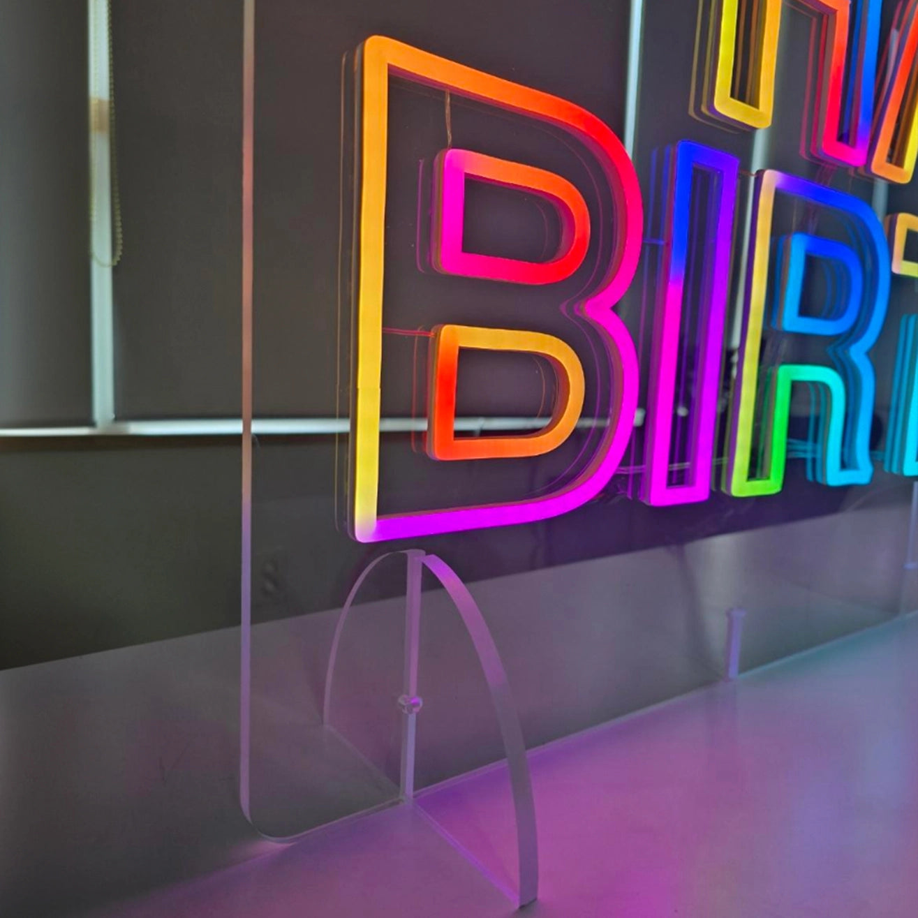 HAPPY BIRTHDAYロゴのネオン看板。製品を支える透明アクリル立て台のアップ画像。製品サイズ1200×500mmに合わせて立て台サイズを製作。