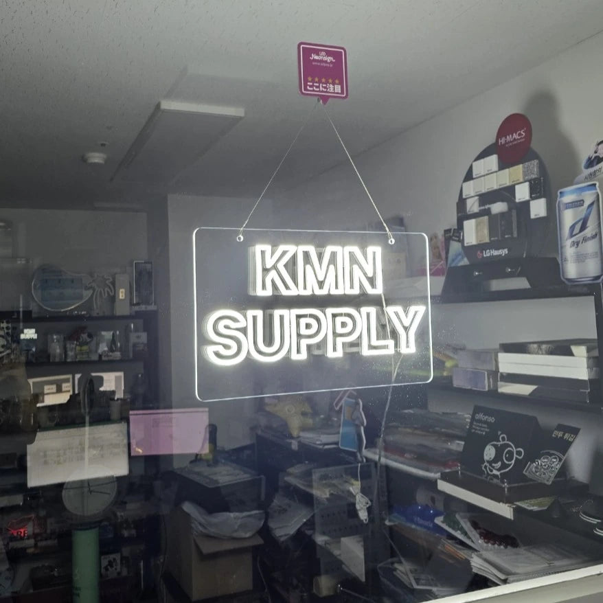 KMNSUPPLYロゴのLEDネオンサイン看板。暗い室内で窓ガラスタイプをガラスに設置して左から見たアングル。