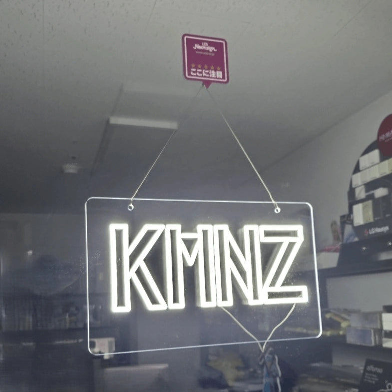 KMNZロゴのLEDネオンサイン看板。窓ガラスタイプをガラスに設置して左斜めから見た全体写真。