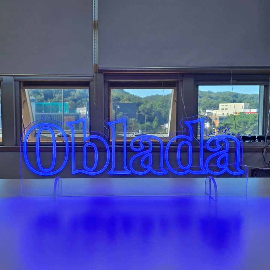 「Oblada」の文字ロゴをブルーのネオンチューブで輪郭に沿って表現したLEDネオンサイン。透明アクリルを使用し、自立式スタンドと天井からの吊り下げ設置の両方に対応した兼用タイプのオリジナル製作例。
