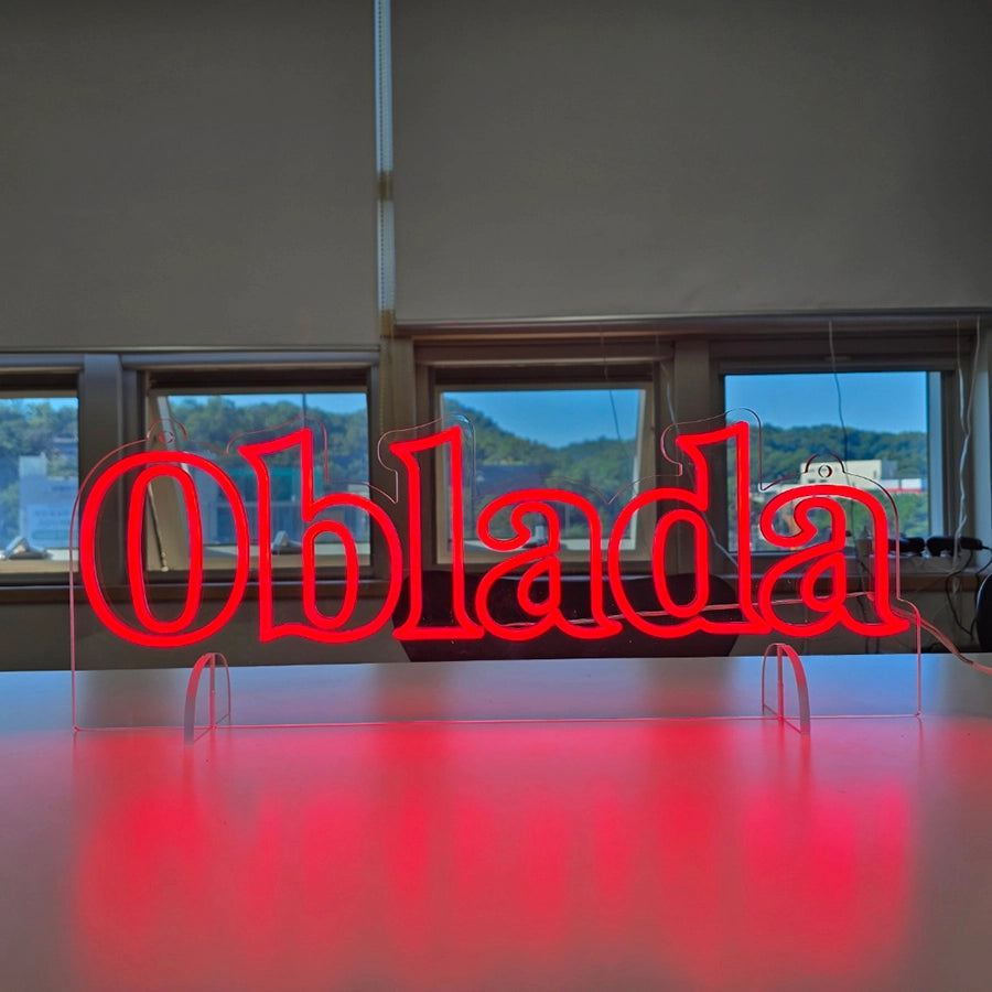 「Oblada」の文字ロゴを鮮やかなレッドのネオンチューブで輪郭に沿って表現したLEDネオンサイン。透明アクリルを使用し、自立式スタンドと天井からの吊り下げ設置の両方に対応した兼用タイプのオリジナル製作例。