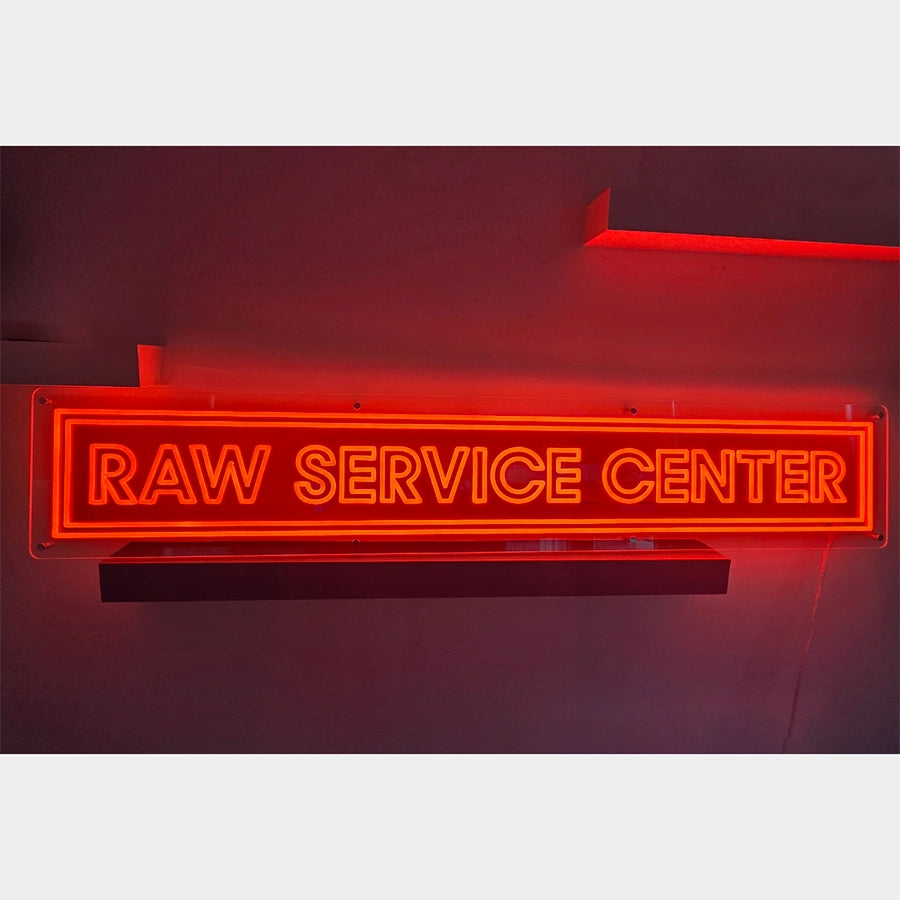 RAW SERVICE CENTERロゴのネオン看板。目を引くオレンジカラーで発光。ビス(ネジ)8個を使用し壁面に設置するタイプ。電源コードは下部出しの白仕様。