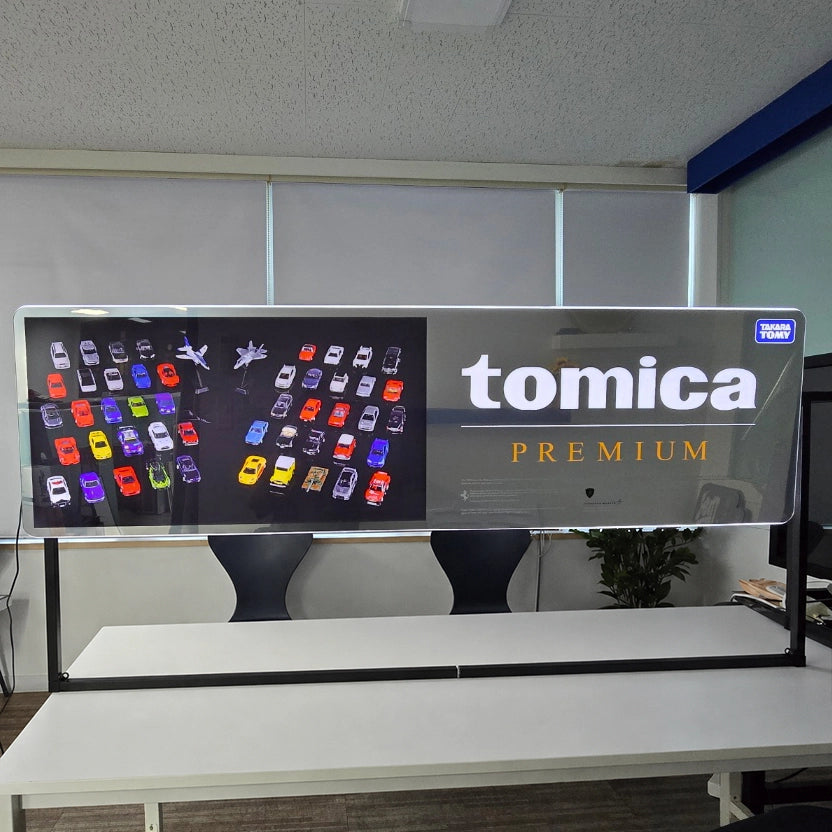 tomica PREMIUMのロゴをFFL（自由形状曲線ライト）で表現した特注LED看板。ロゴデザインを忠実に再現し、背景にミラー素材を採用した視認性の高いオーダーメイドライトサイン。