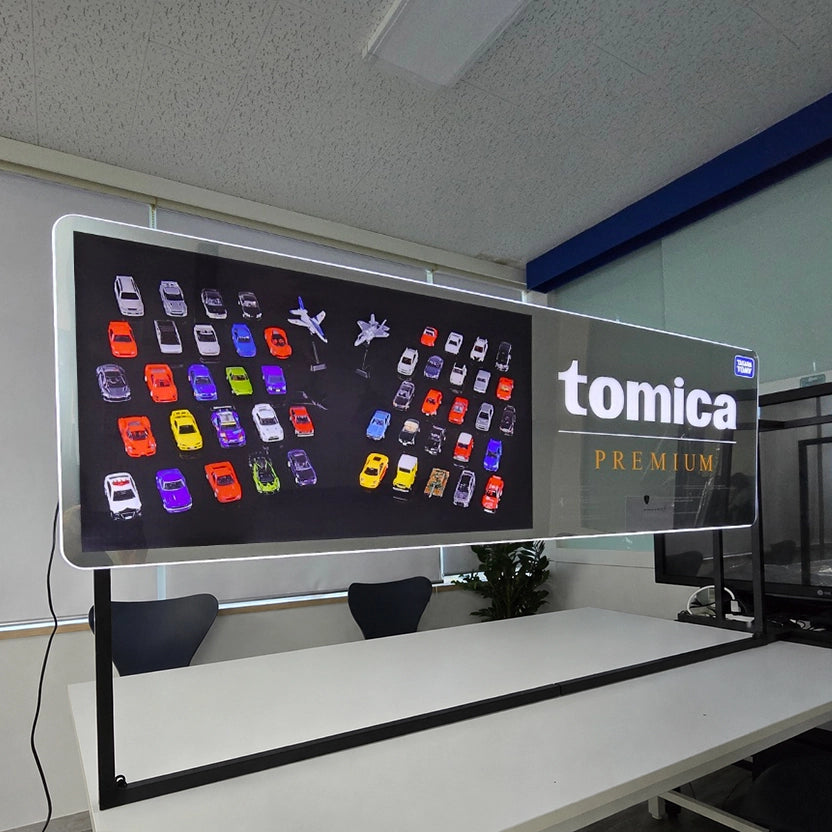 tomica PREMIUMのロゴをFFL（自由形状曲線ライト）で表現した特注LED看板。ロゴ部分と側面がLEDで発光する、ご発注者様のご希望に合わせた四角形デザインのオーダーメイドライトサイン。